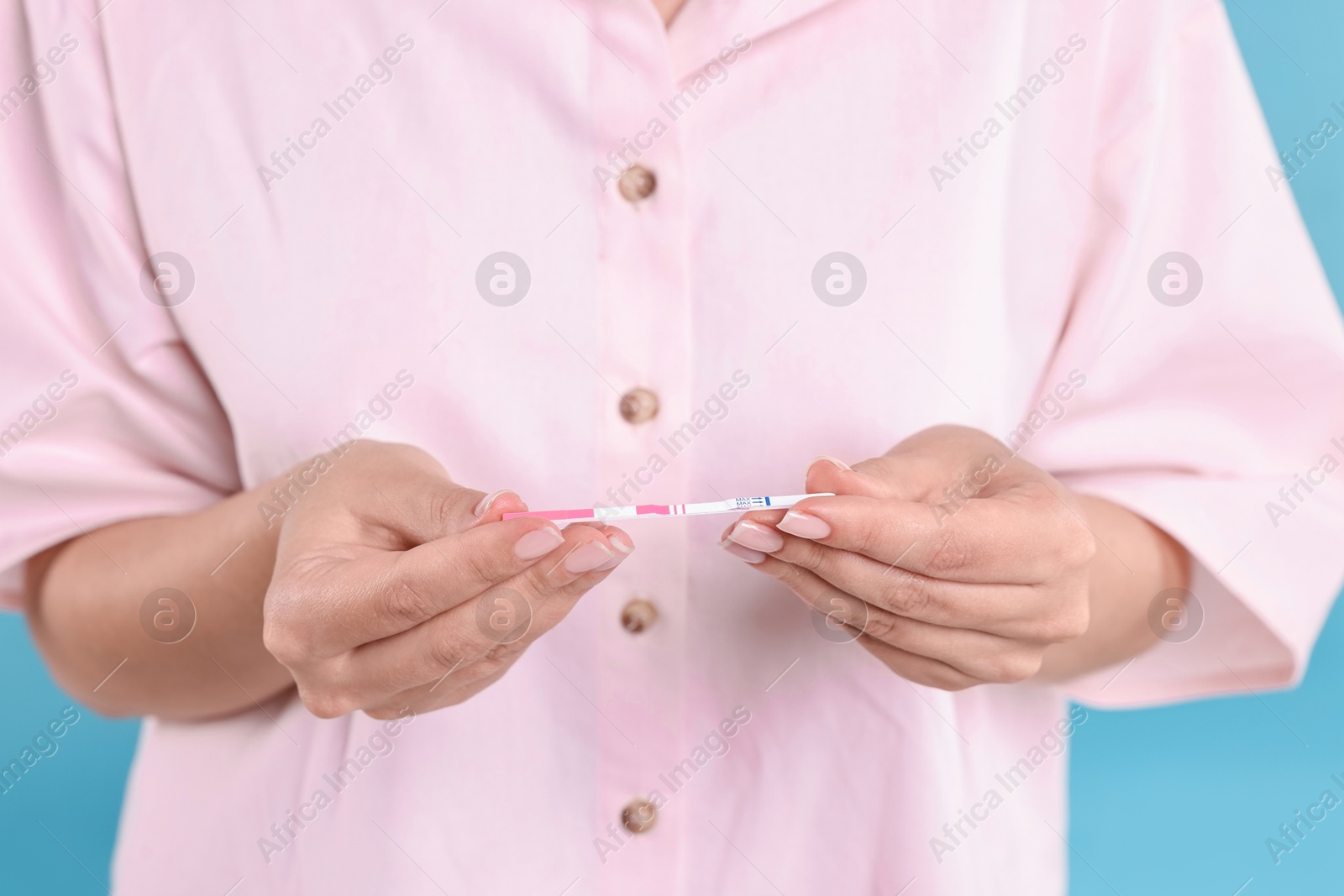 Photo of Young woman with pregnancy test on light blue background, closeup