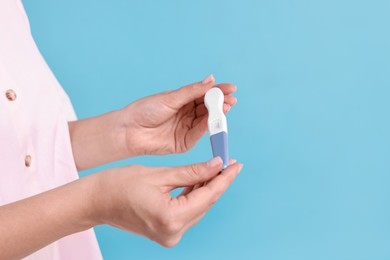 Photo of Young woman with pregnancy test on light blue background, closeup. Space for text