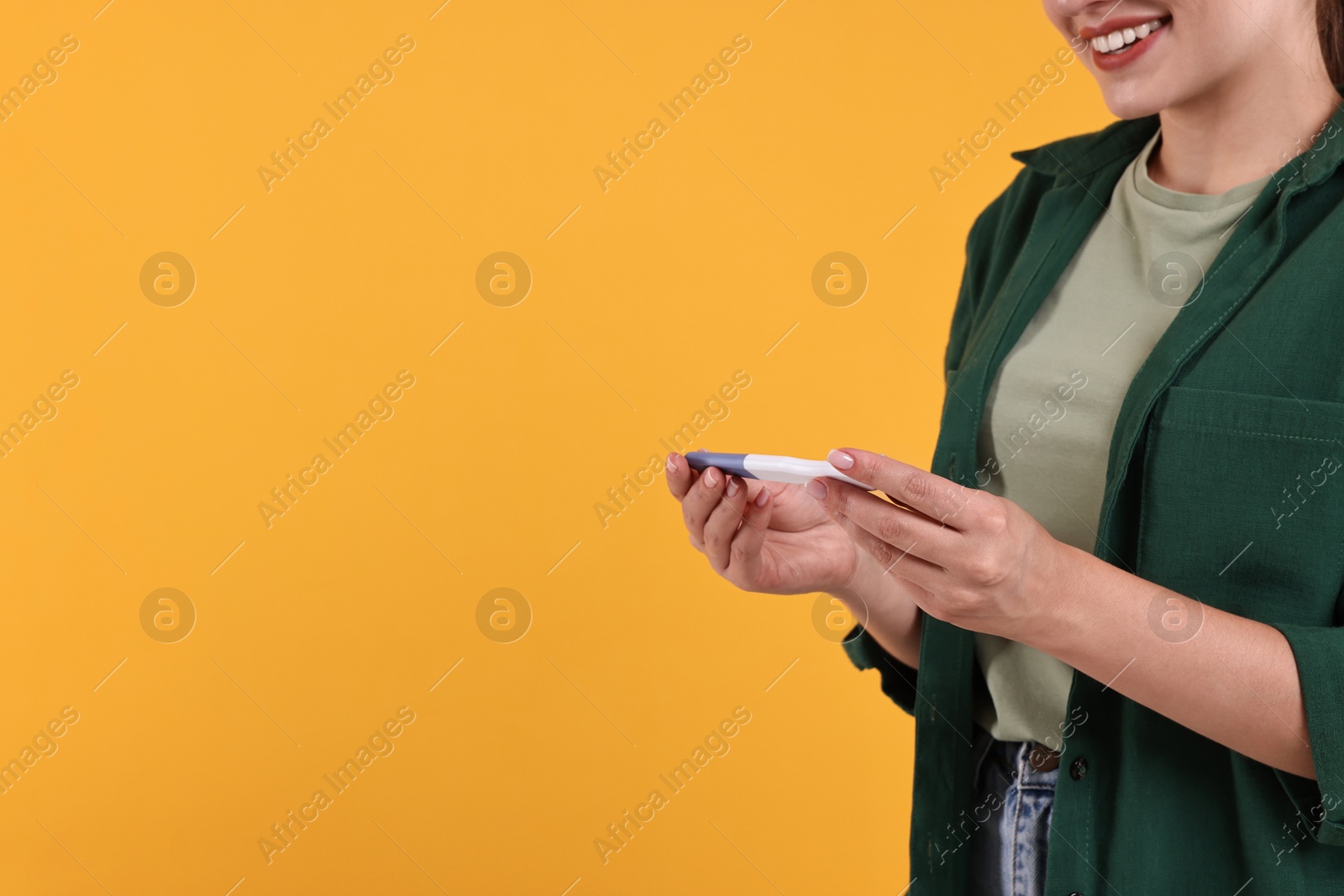 Photo of Happy young woman with pregnancy test on orange background, space for text