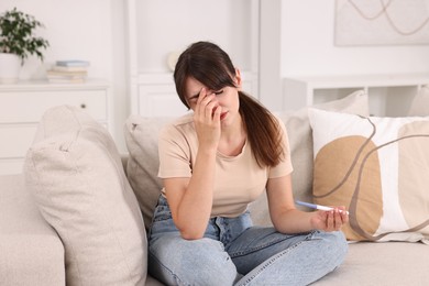 Photo of Worried young woman with pregnancy test on sofa at home