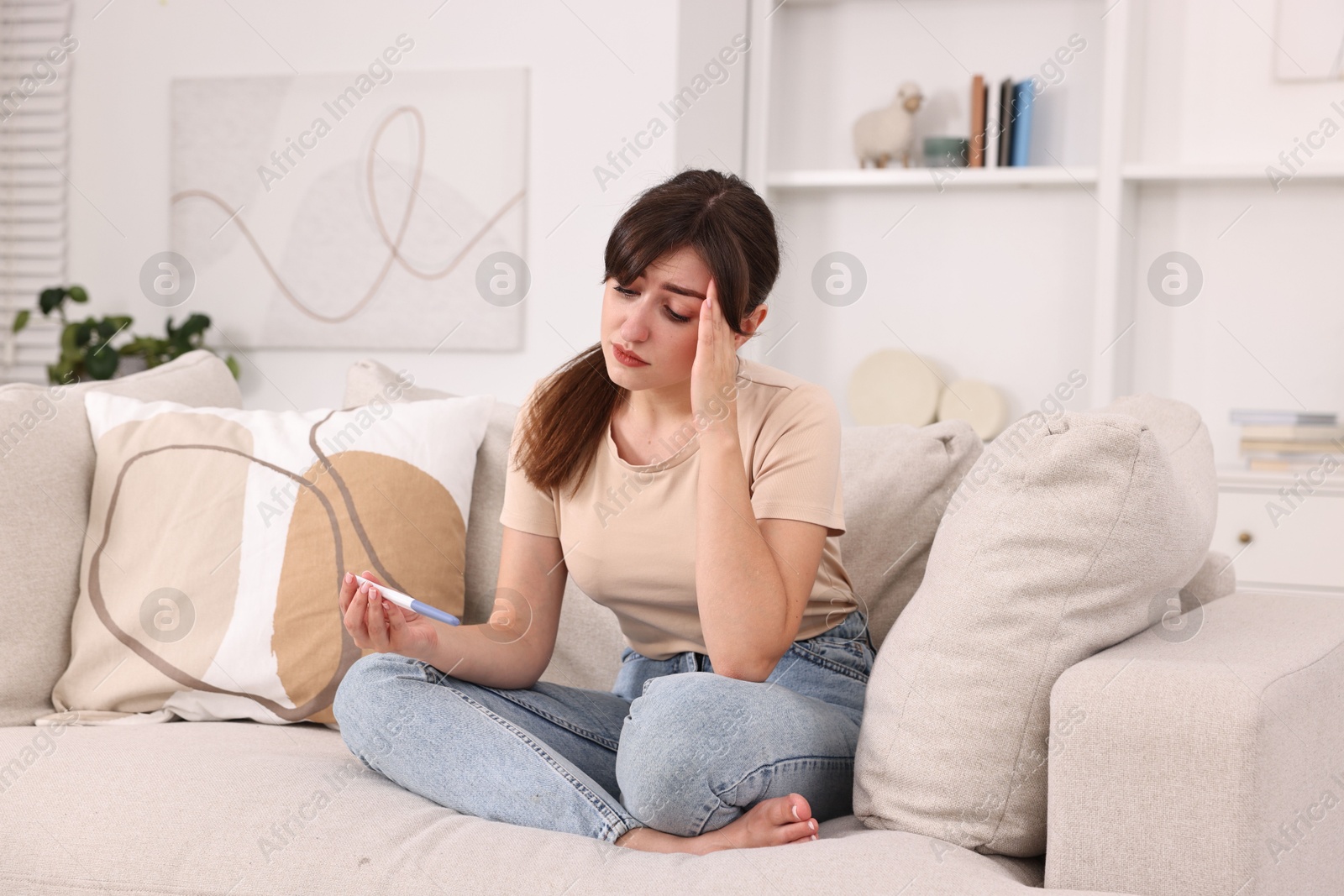 Photo of Worried young woman with pregnancy test on sofa at home