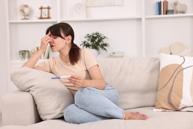 Photo of Worried young woman with pregnancy test on sofa at home