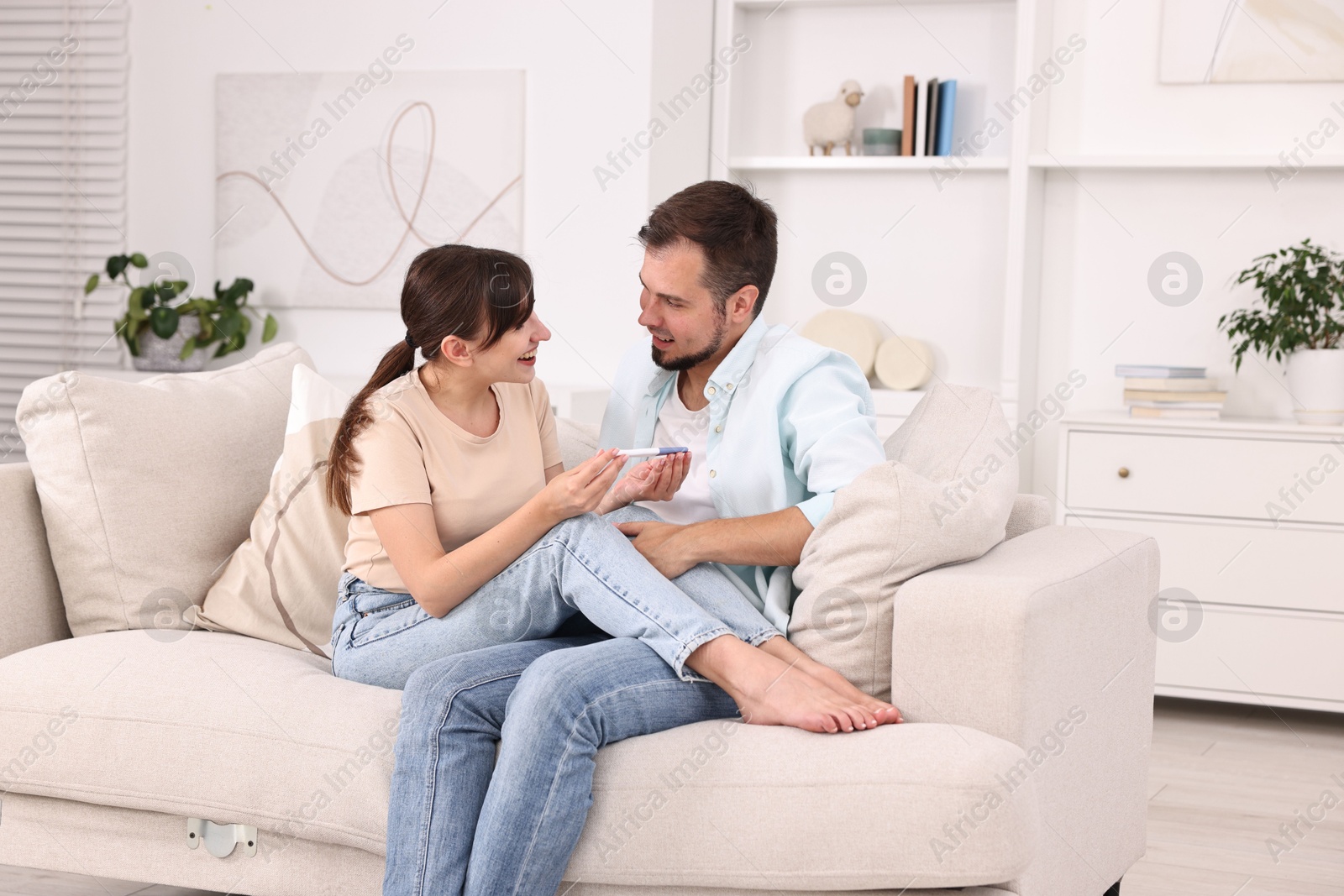 Photo of Happy young couple with pregnancy test on sofa at home