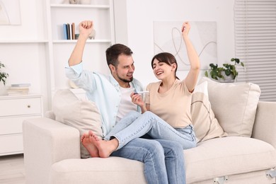 Photo of Happy young couple with pregnancy test on sofa at home