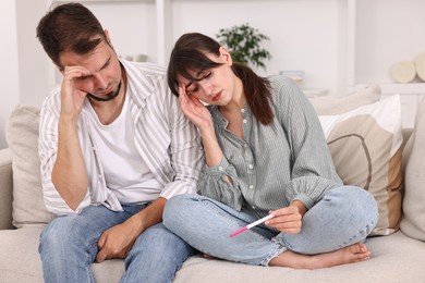 Photo of Worried young couple with pregnancy test on sofa at home