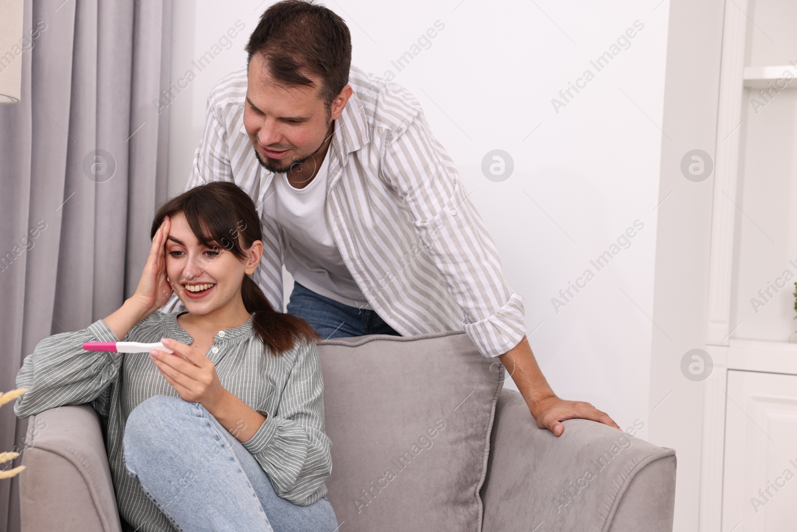 Photo of Happy young couple with pregnancy test at home, space for text