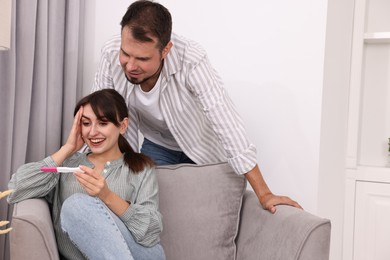 Happy young couple with pregnancy test at home, space for text