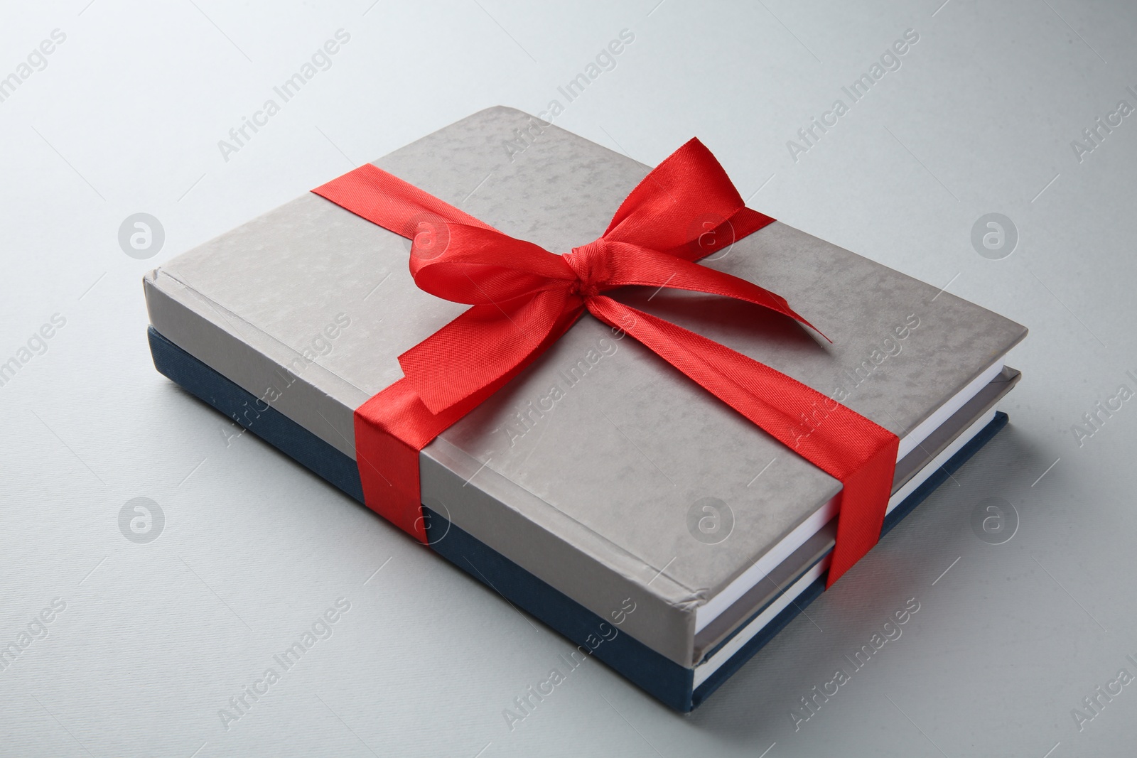 Photo of Books tied with red ribbon on grey background, closeup. Perfect gift