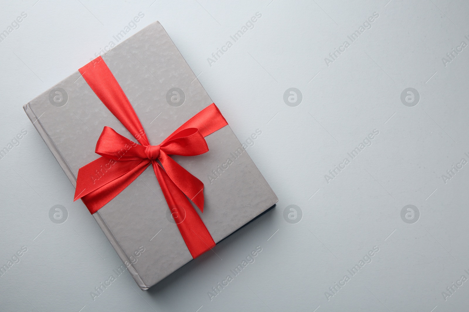 Photo of Book tied with red ribbon on grey background, top view with space for text. Perfect gift