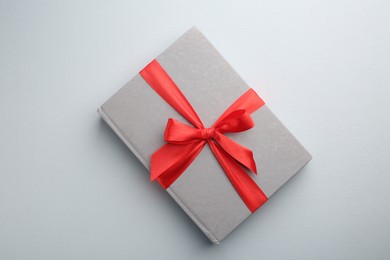 Photo of Book tied with red ribbon on grey background, top view. Perfect gift