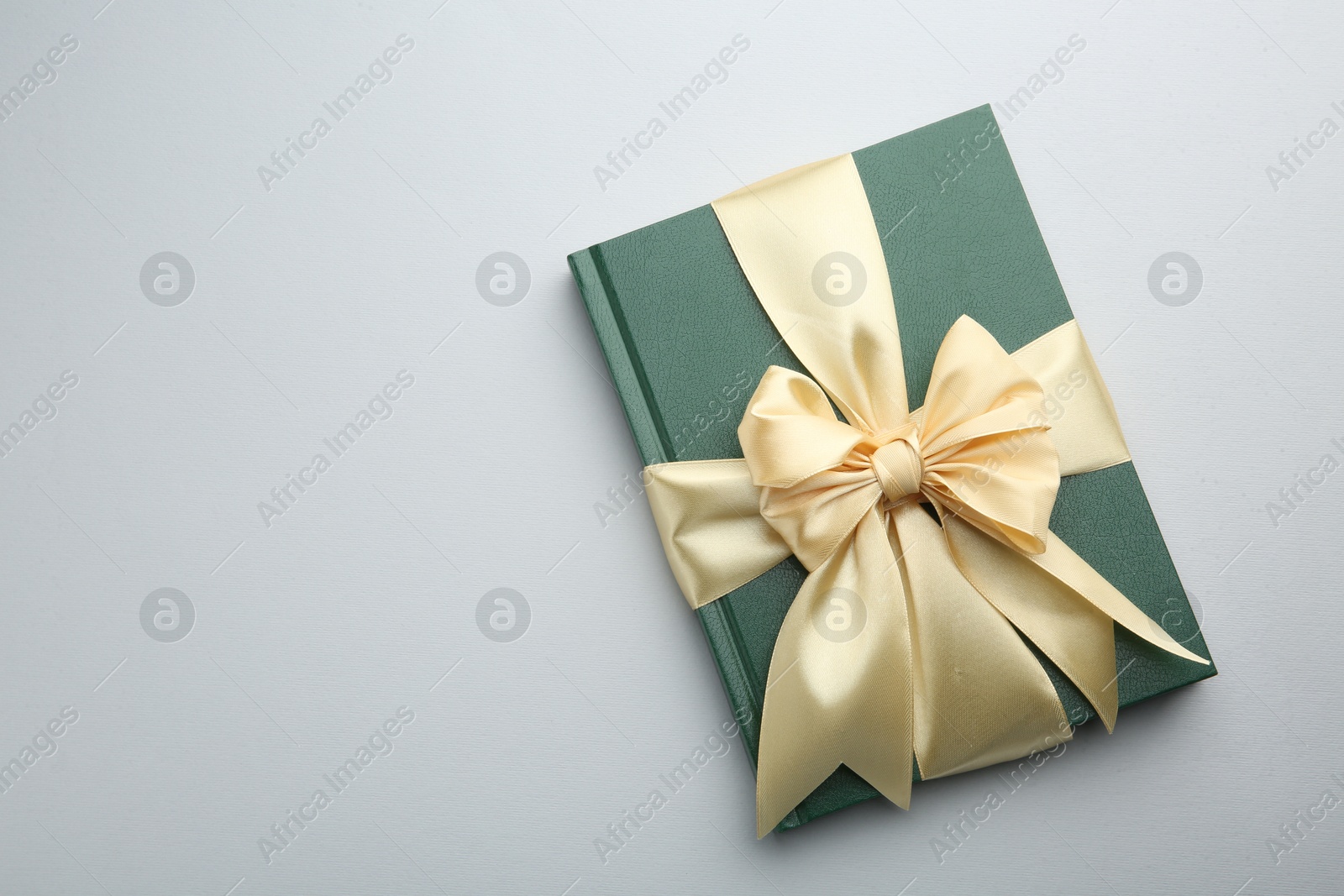 Photo of Book tied with golden ribbon on grey background, top view with space for text. Perfect gift