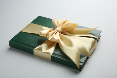 Photo of Book tied with golden ribbon on grey background, closeup. Perfect gift