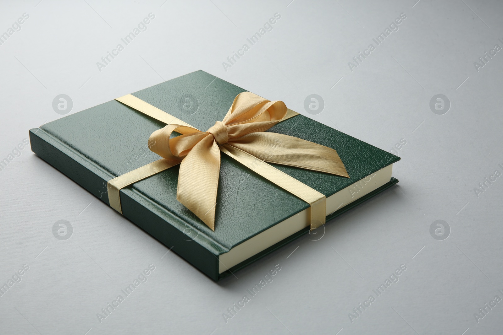 Photo of Book tied with golden ribbon on grey background. Perfect gift