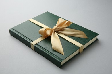 Book tied with golden ribbon on grey background, closeup. Perfect gift