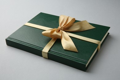 Photo of Book tied with golden ribbon on grey background, closeup. Perfect gift