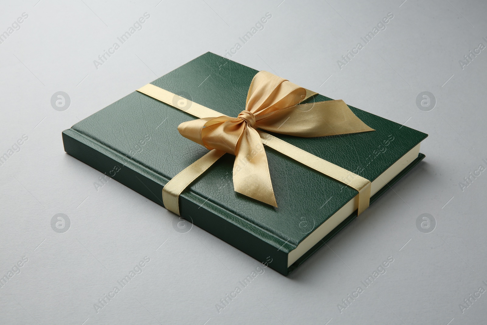 Photo of Book tied with golden ribbon on grey background. Perfect gift