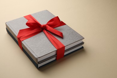 Photo of Books tied with red ribbon on beige background, closeup. Perfect gift