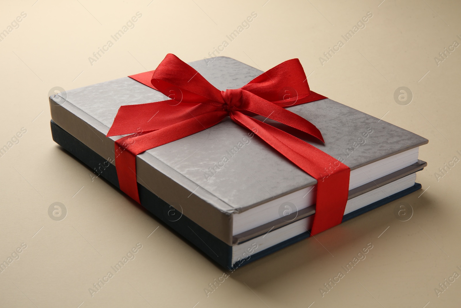 Photo of Books tied with red ribbon on beige background, closeup. Perfect gift