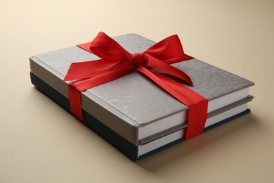 Books tied with red ribbon on beige background, closeup. Perfect gift