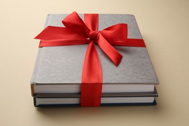 Photo of Books tied with red ribbon on beige background, closeup. Perfect gift