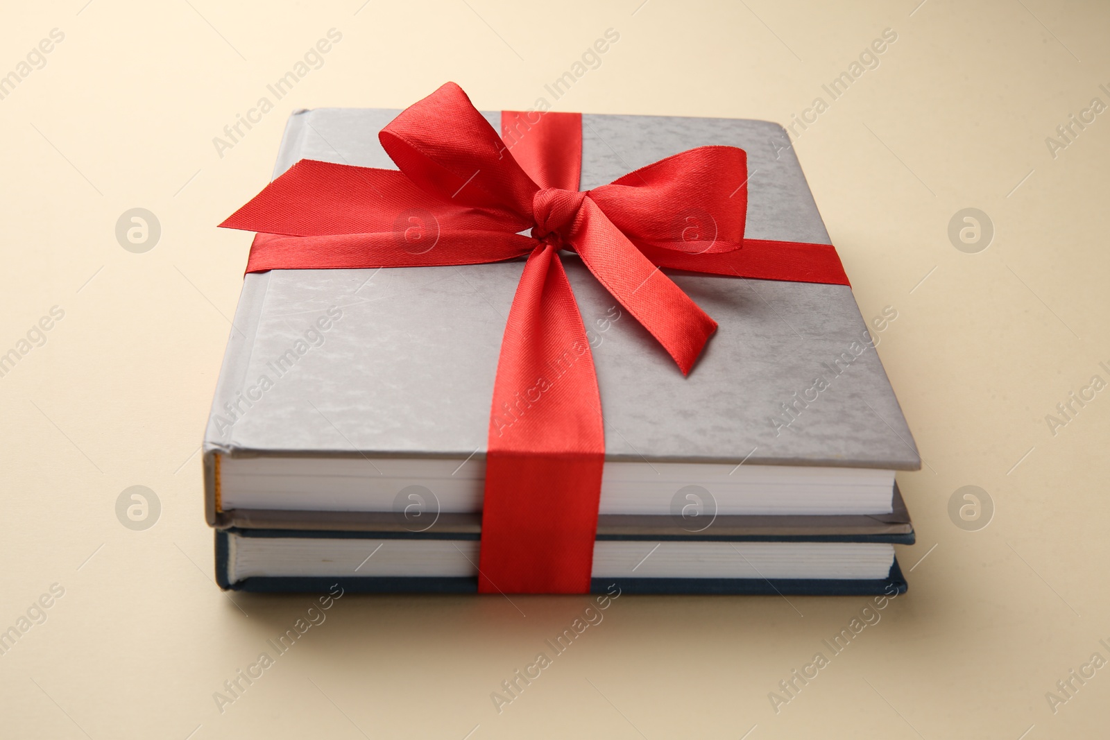 Photo of Books tied with red ribbon on beige background, closeup. Perfect gift