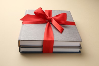 Books tied with red ribbon on beige background, closeup. Perfect gift