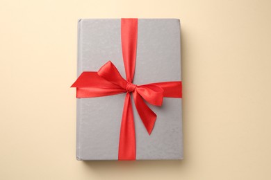 Photo of Book tied with red ribbon on beige background, top view. Perfect gift