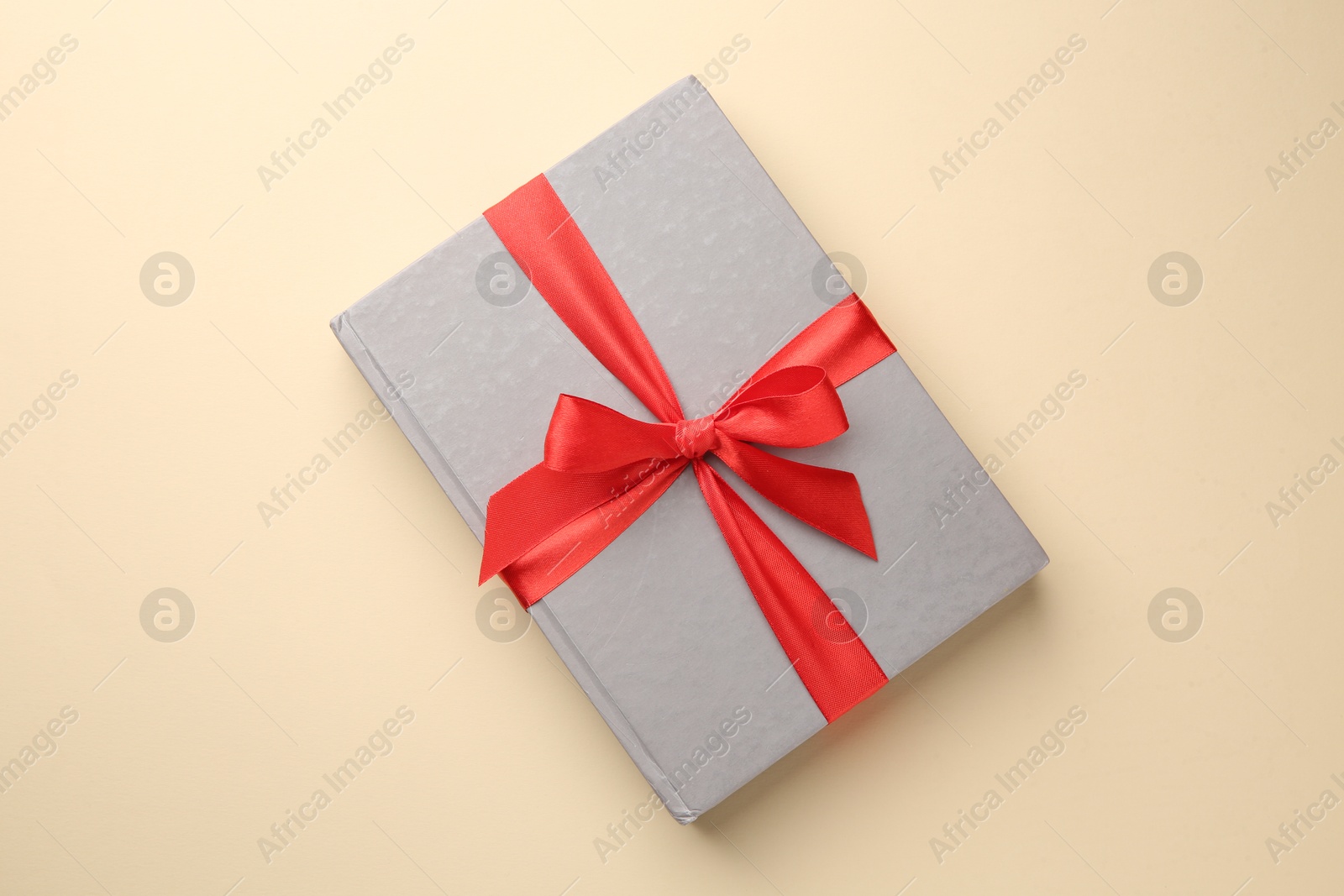 Photo of Book tied with red ribbon on beige background, top view. Perfect gift