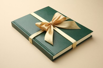 Photo of Book tied with golden ribbon on beige background, closeup. Perfect gift