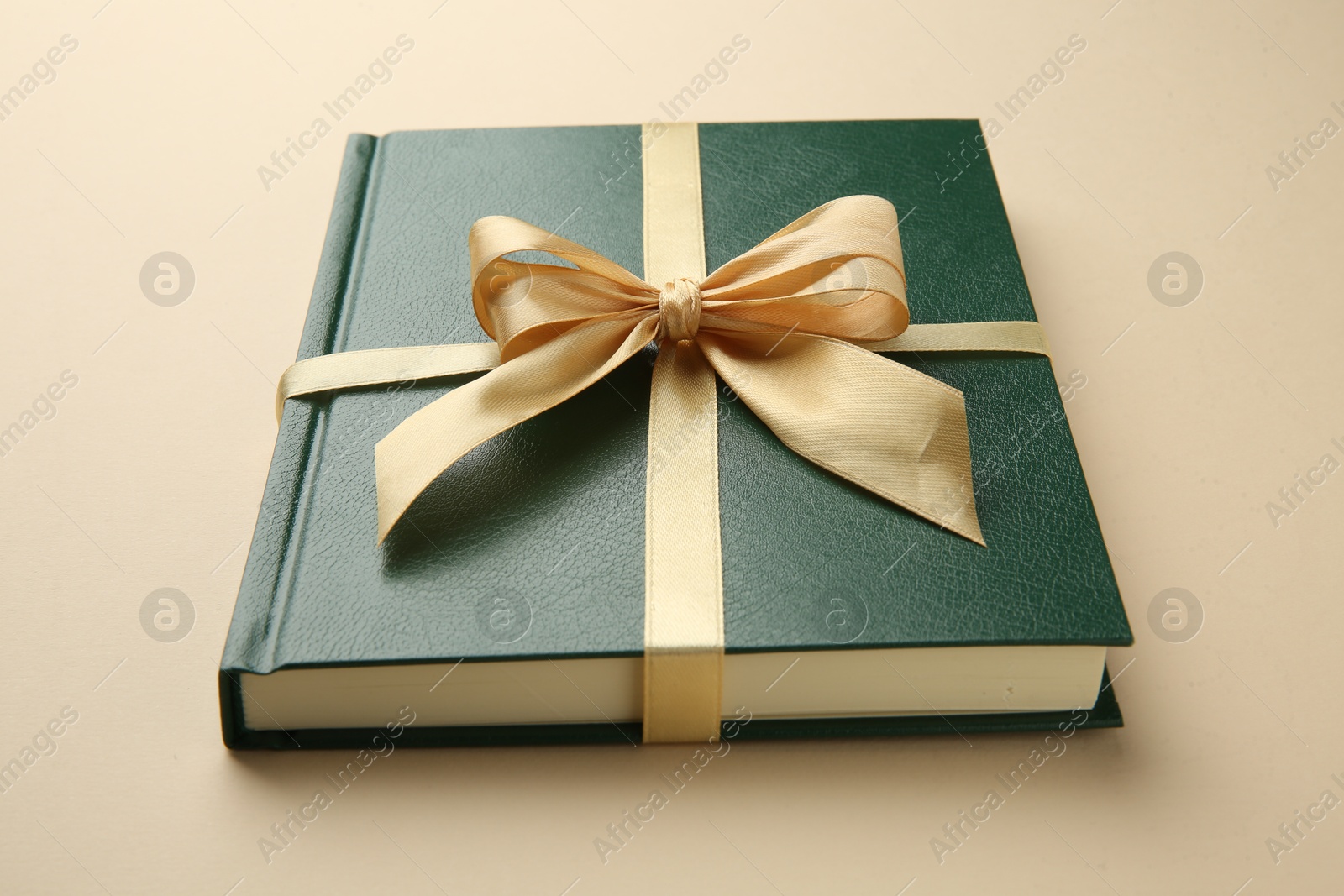 Photo of Book tied with golden ribbon on beige background, closeup. Perfect gift