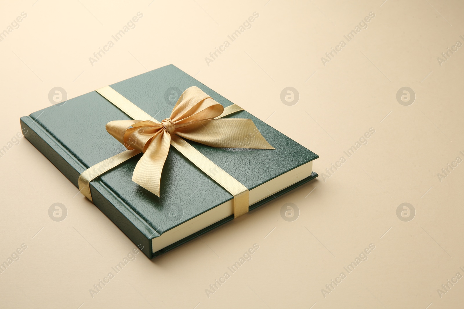 Photo of Book tied with golden ribbon on beige background. Perfect gift