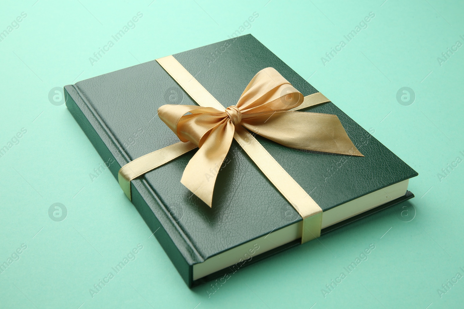 Photo of Book tied with golden ribbon on green background, closeup. Perfect gift