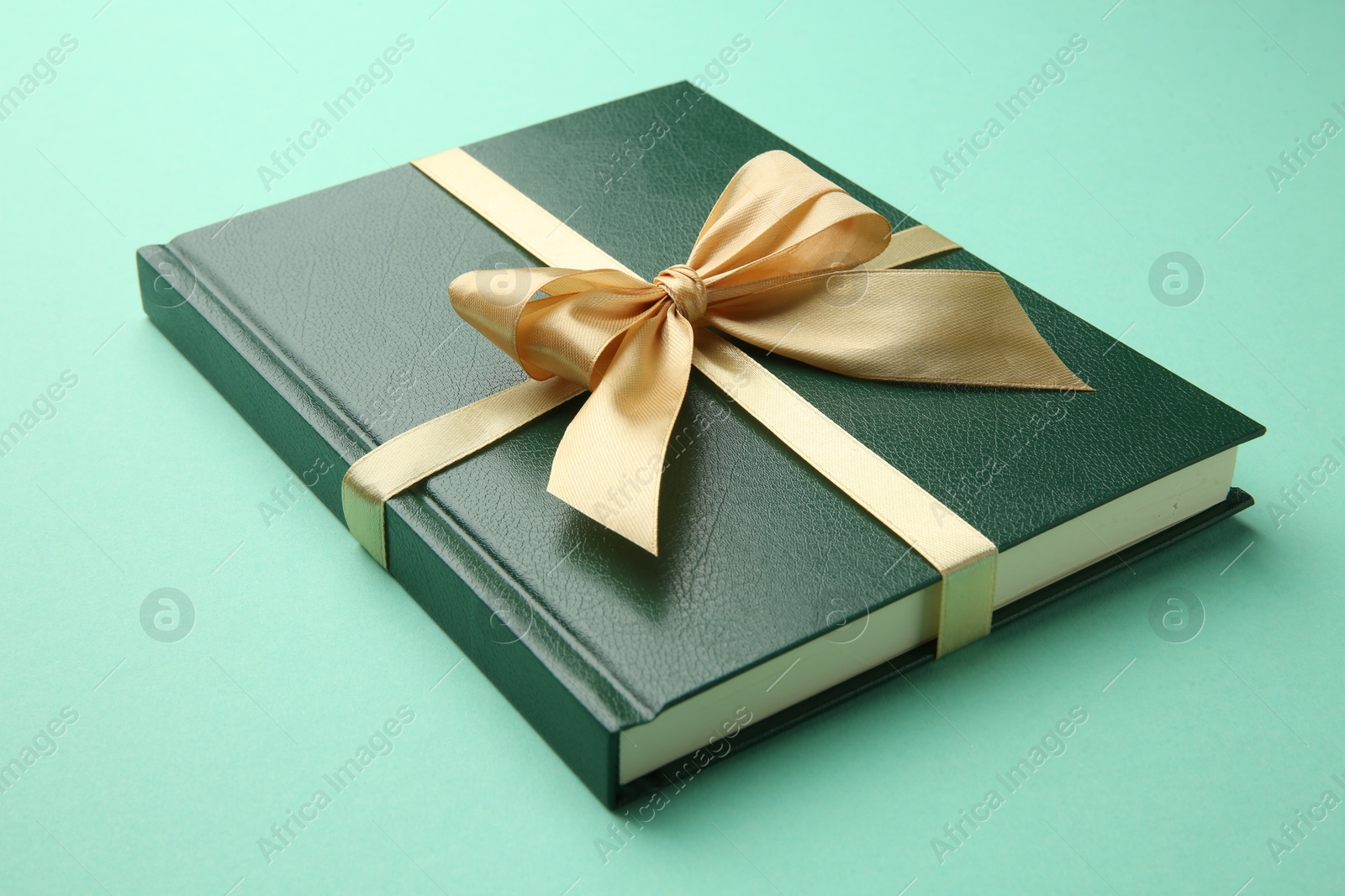 Photo of Book tied with golden ribbon on green background, closeup. Perfect gift