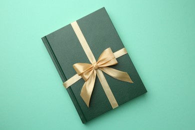 Book tied with golden ribbon on green background, top view. Perfect gift