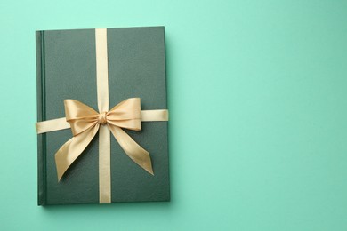 Photo of Book tied with golden ribbon on green background, top view with space for text. Perfect gift