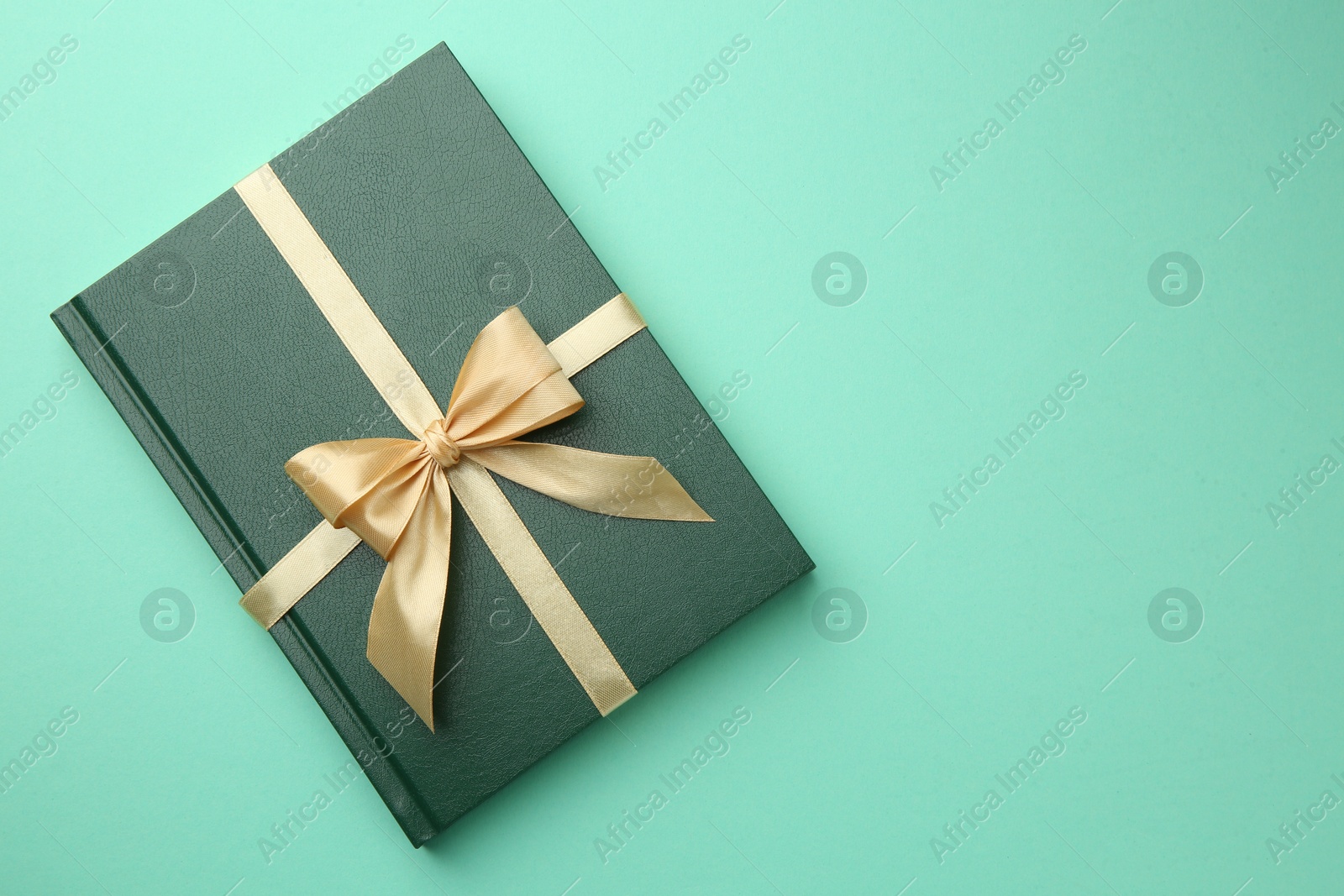 Photo of Book tied with golden ribbon on green background, top view with space for text. Perfect gift