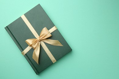 Photo of Book tied with golden ribbon on green background, top view with space for text. Perfect gift