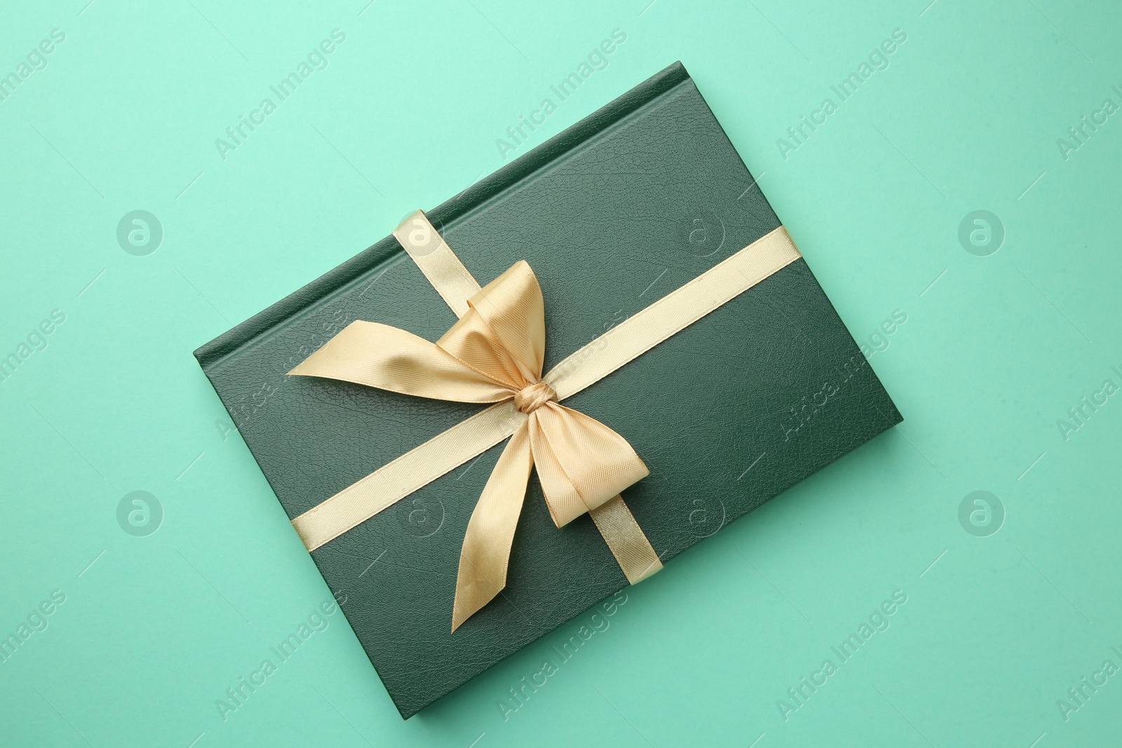 Photo of Book tied with golden ribbon on green background, top view. Perfect gift