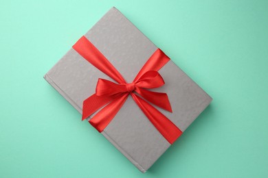 Photo of Book tied with red ribbon on green background, top view. Perfect gift