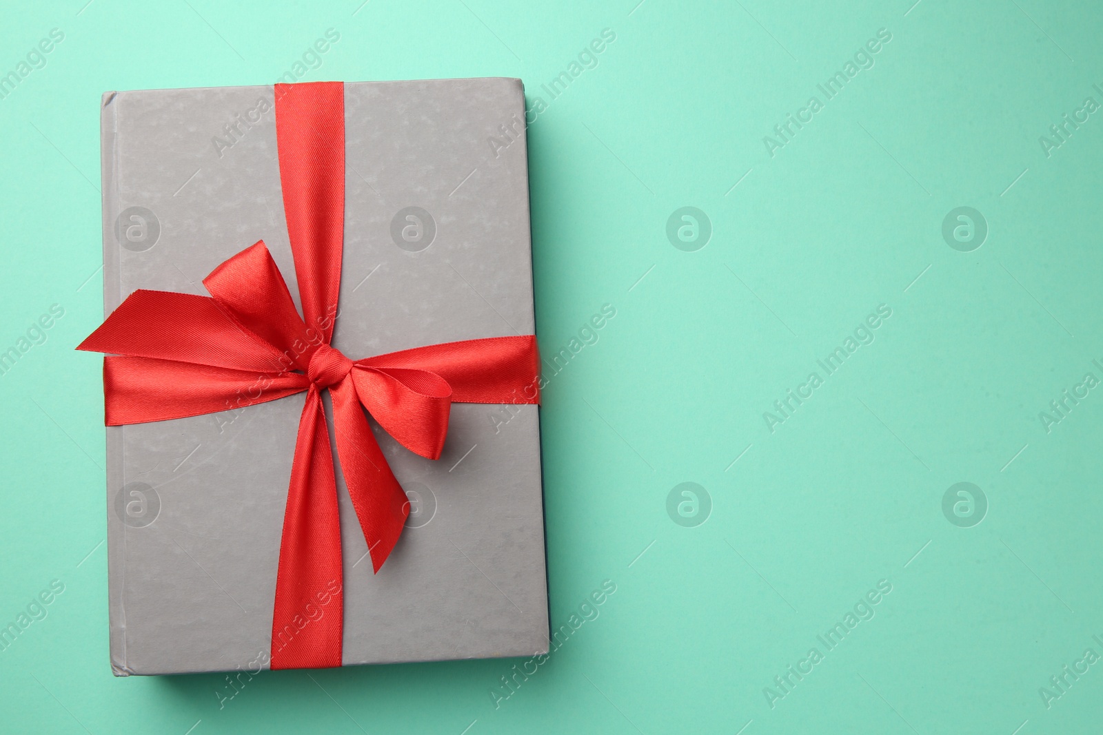 Photo of Book tied with red ribbon on green background, top view with space for text. Perfect gift