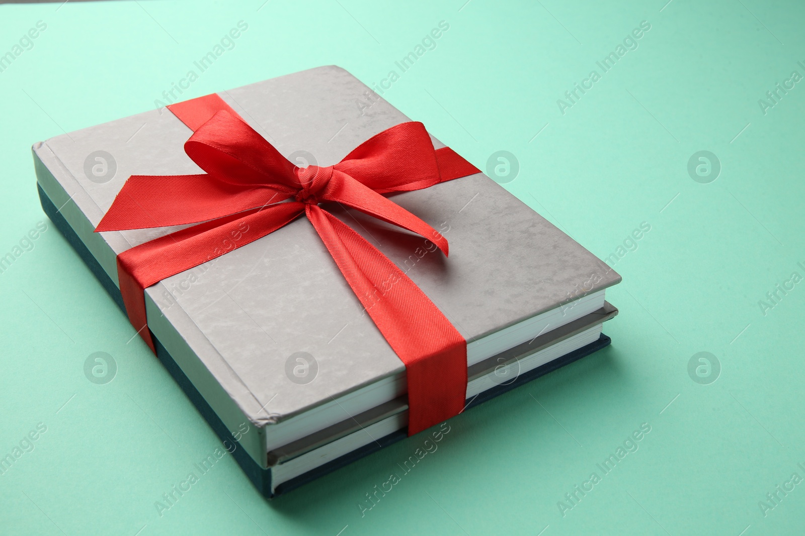 Photo of Books tied with red ribbon on green background, closeup. Perfect gift