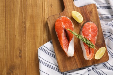 Photo of Fresh salmon steaks, lemon and rosemary on wooden table, top view. Space for text