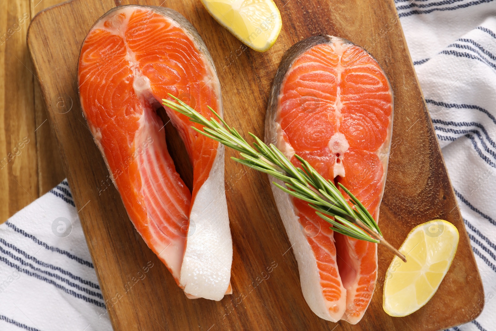 Photo of Fresh salmon steaks, lemon and rosemary on wooden table, top view