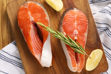 Photo of Fresh salmon steaks, lemon and rosemary on wooden table, top view