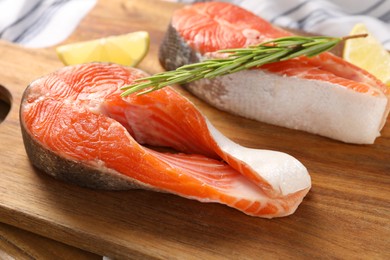 Photo of Board with fresh salmon steaks, lemon and rosemary on table, closeup