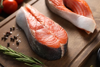 Board with fresh salmon steaks, rosemary and peppercorns on table, closeup