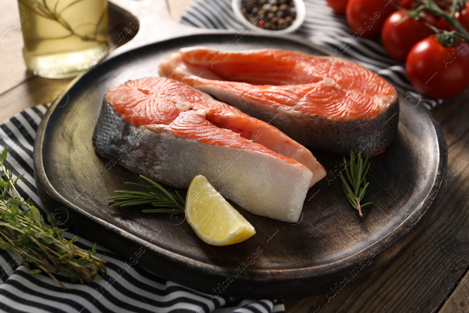 Photo of Board with fresh salmon steaks, lemon and rosemary on wooden table, closeup