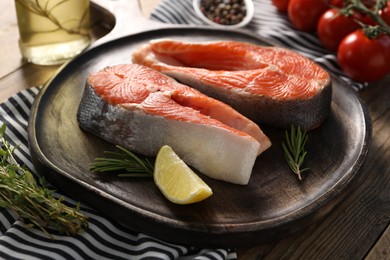 Board with fresh salmon steaks, lemon and rosemary on wooden table, closeup