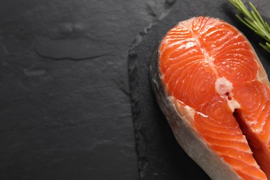 Photo of Fresh salmon steak and rosemary on dark textured table, above view. Space for text