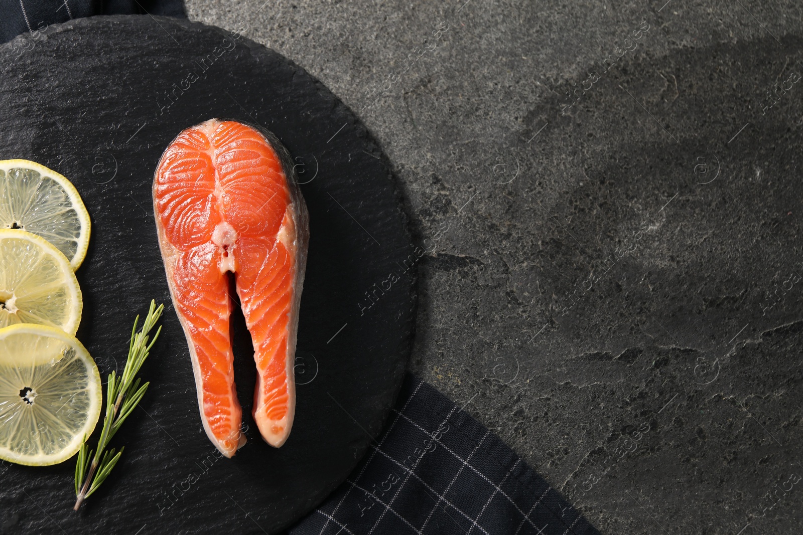 Photo of Fresh salmon steak, rosemary and lemon on dark textured table, top view. Space for text